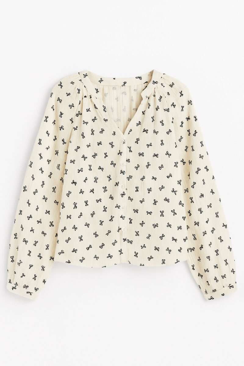 Blouse en gaze de coton femme coupe fluide, idéale pour un look bohème chic. Tissu crème texturé avec motif de nœuds brodés noirs. Manches longues et col V fendu.